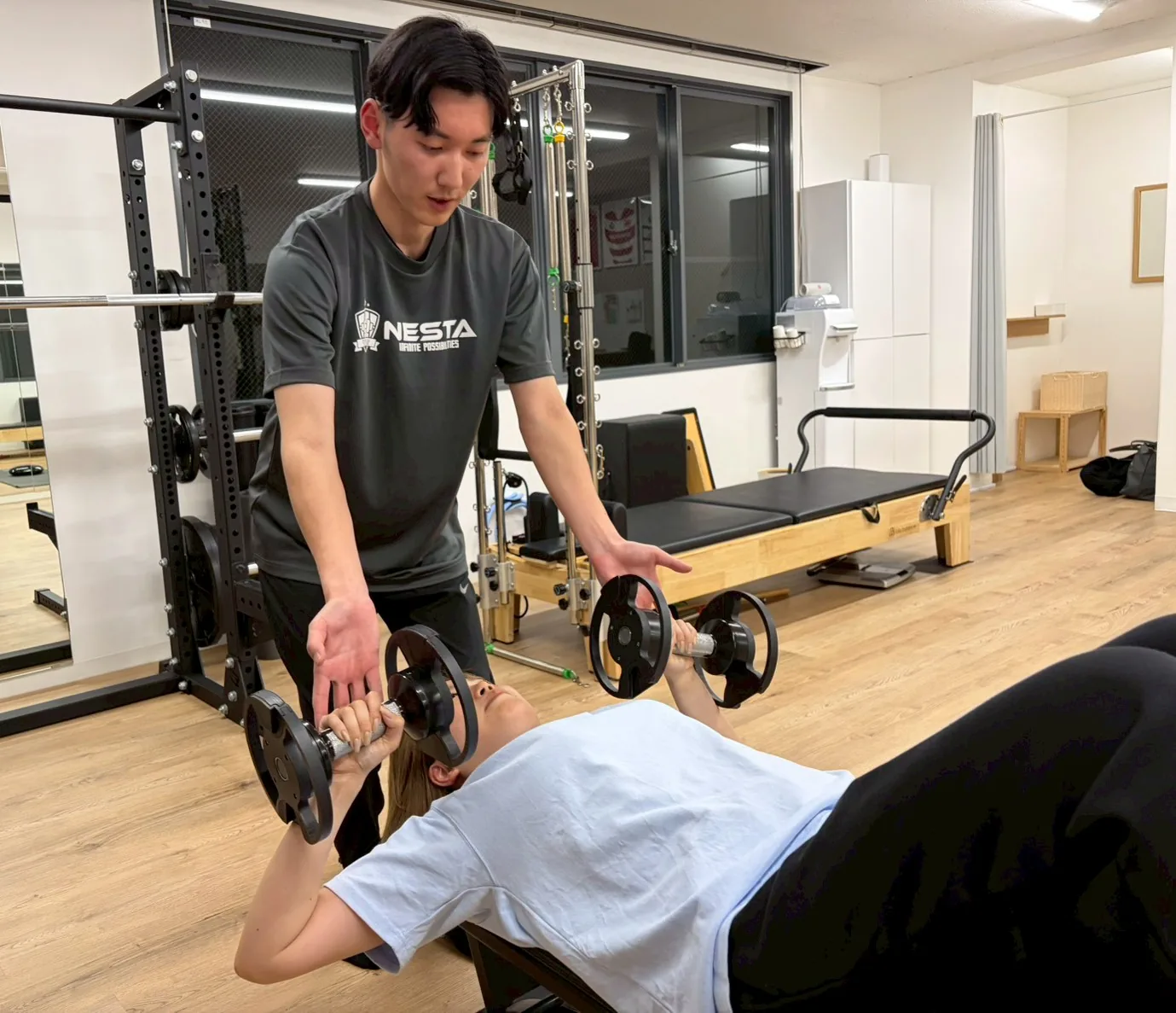 ダンベルプレスの動きをトレーナーが後ろから補助している様子
