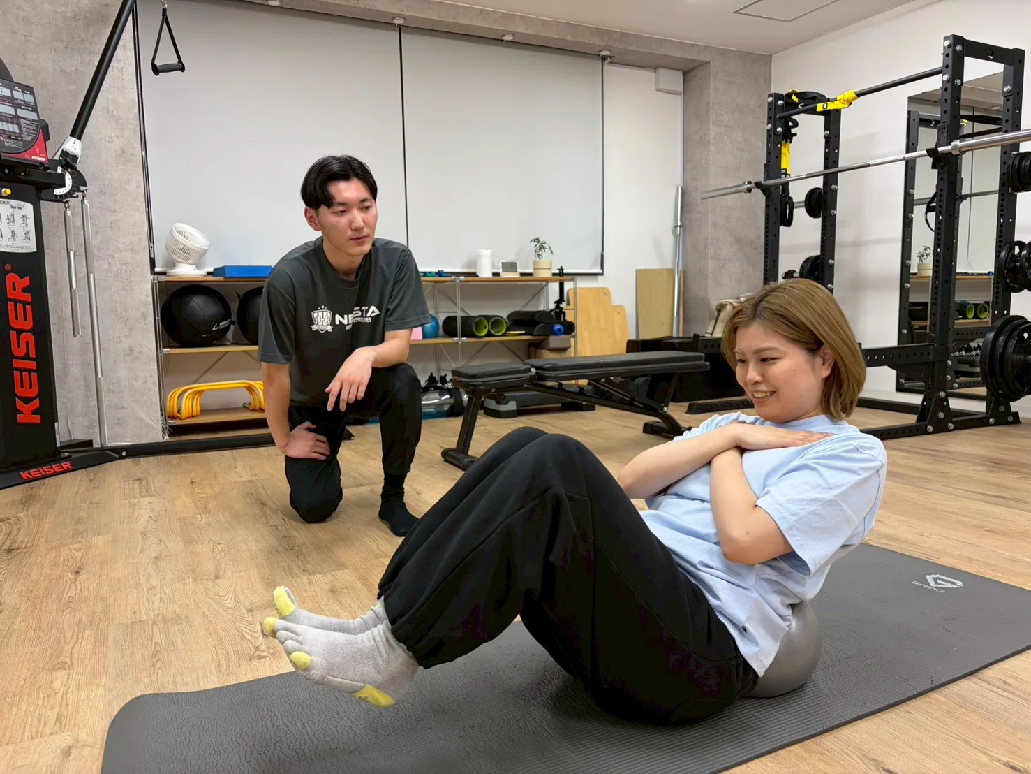 マットでの腹筋種目をトレーナーが横について指導している様子