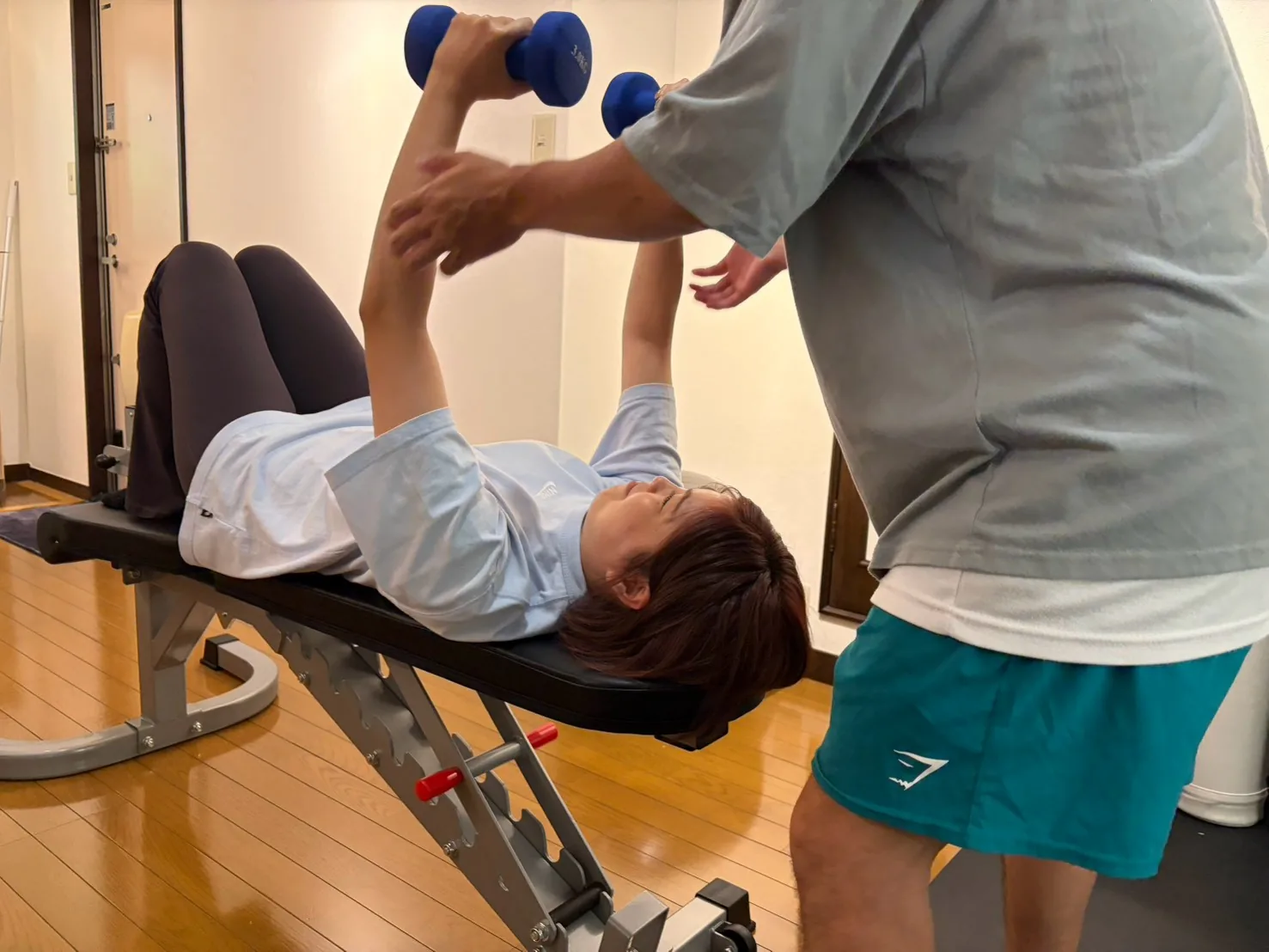 ダンベルプレスの軌道をトレーナーが補助している様子