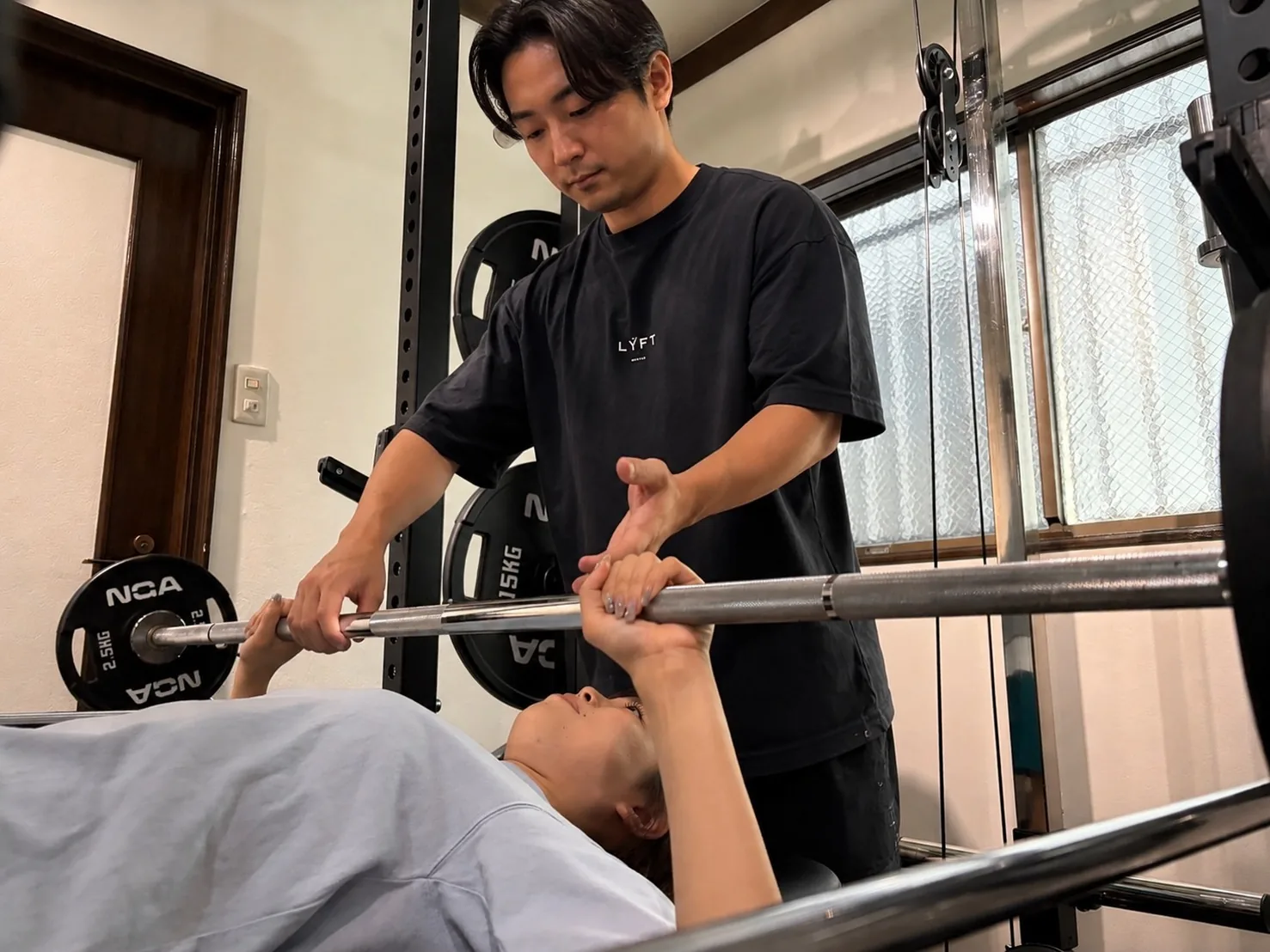 ベンチプレスのバーを、トレーナーが上から支えてフォームを確認している様子